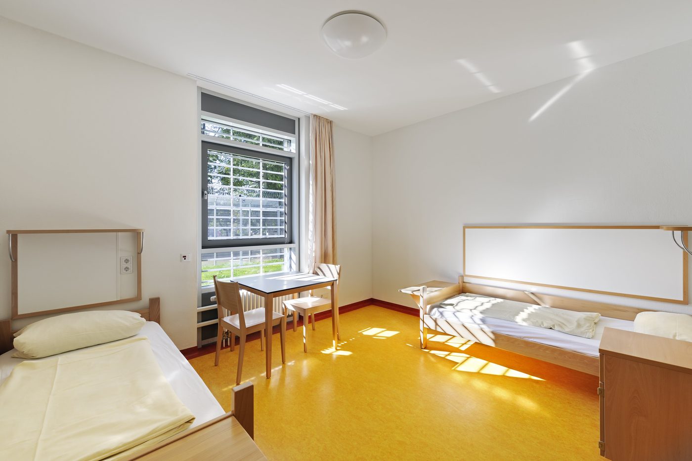 Patientenzimmer mit gelbem Boden und Holzmöbeln
